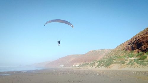 Person paragliding by sea against sky