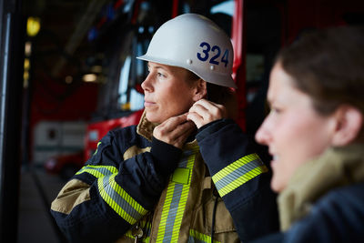 Female firefighter wearing helmet while standing with coworker in fire station