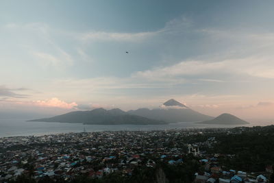 Aerial view of city by sea against sky during sunset