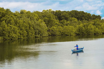 Fisherman fishing in lake while standing on boat against trees