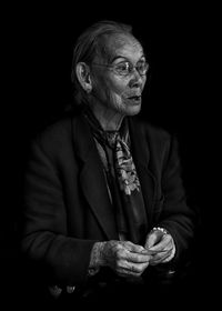 Senior woman looking away while sitting against black background