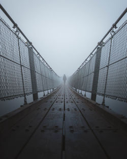 Person walking on suspension bridge in foggy weather