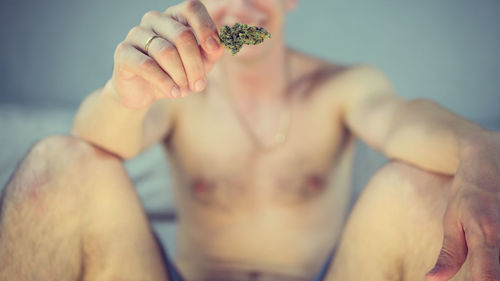 Midsection of shirtless man holding marijuana