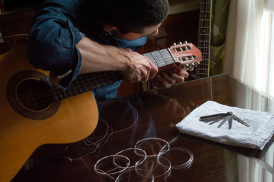 Man adjusting strings in guitar on table at home