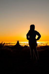 Silhouette woman standing on landscape against orange sky