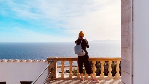 Rear view of woman with backpack looking at sea while standing in balcony against sky