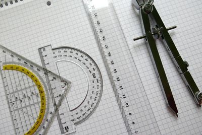 Close-up of set square and protractor with drawing compass by ruler on book