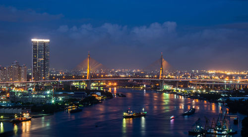 Illuminated city by river against sky