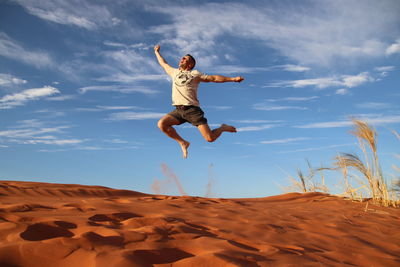 Low angle view of man jumping at desert against blue sky