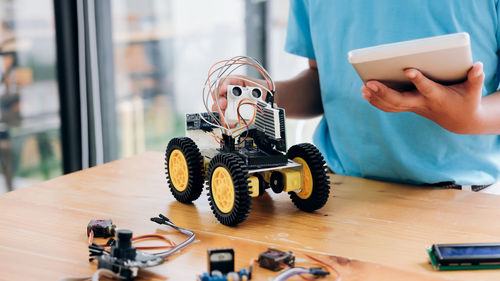 Midsection of boy using digital tablet while repairing toy on table