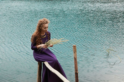 Young woman sitting on railing by lake