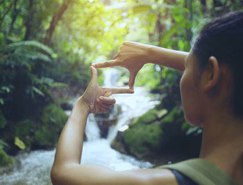 Woman making finger frame against waterfall in forest