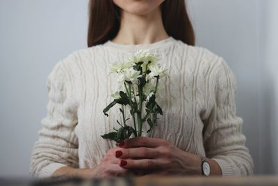 Midsection of woman with flowers against wall