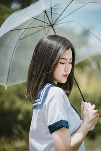 Thoughtful young woman with umbrella standing against sky