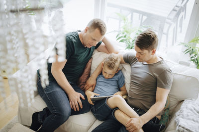 High angle view of homosexual fathers sitting while son using digital tablet at home