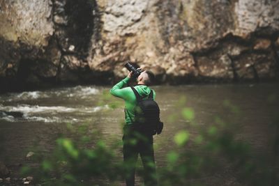 Rear view of man photographing by river