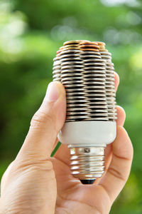 Cropped hand of man holding light bulb against plants