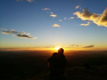 Rear view of silhouette man standing on landscape against sunset sky