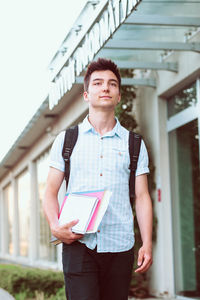 Young university student walking while holding books outdoors