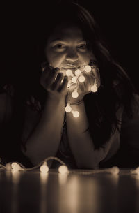 Portrait of young woman with illuminated christmas lights in darkroom