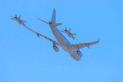 Low angle view of airplanes and fighter jets engaged in mid-air refuelling against clear blue sky