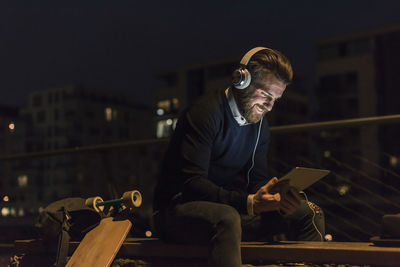 Smiling young man with tablet and headphones in the city at night