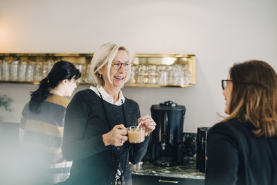 Businesswoman having tea while talking to coworker at office