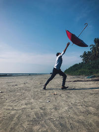Full length of man throwing umbrella mid air at beach