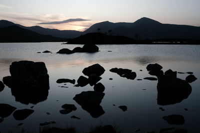 Silhouette rocks on sea shore against sky during sunset