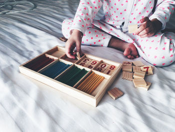 Low section of person arranging toy blocks in wooden box on bed