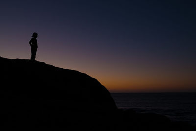 Silhouette man on rock by sea against clear sky during sunset