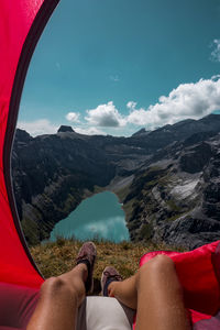 Low section of person in tent on mountains by lake against sky