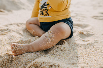 Low section of boy relaxing on sand at beach