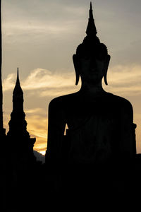 Silhouette of buddha statue against cloudy sky