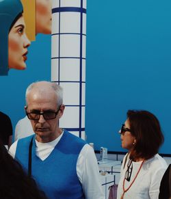 Portrait of man and woman standing against blue wall