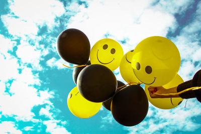 Low angle view of hand holding balloons against sky