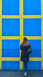A view from the back of a woman with long hair against a checkered wall of blue and yellow