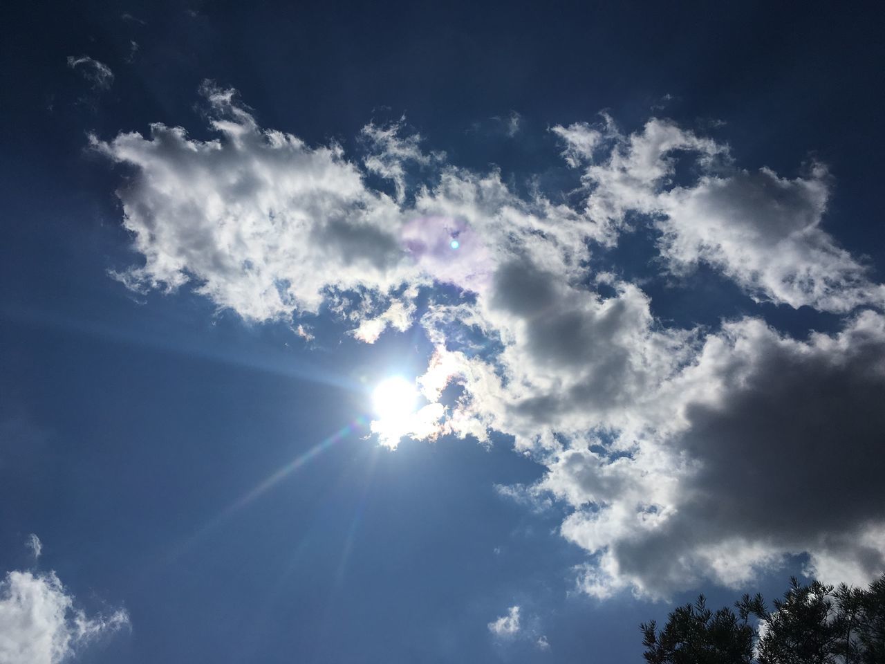 LOW ANGLE VIEW OF SUNLIGHT STREAMING THROUGH CLOUDS IN SKY