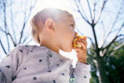 Low angle view of girl eating food against tree