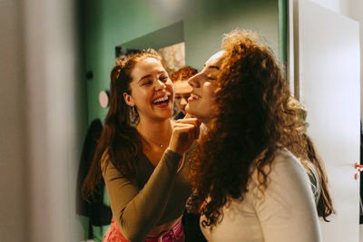 Cheerful young woman helping friend with make-up at home
