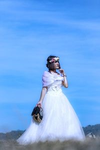 Bride wearing flowers while looking away on land against blue sky