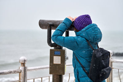 Man standing by railing against sea during winter against sky