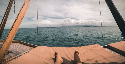Low section of man lying on sailboat sailing in sea against sky