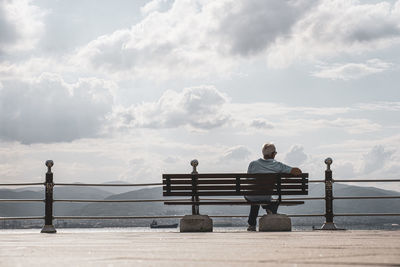 Rear view of man sitting on bench against sky