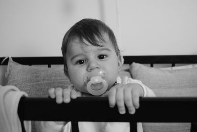 Portrait of cute baby girl sucking pacifier in crib