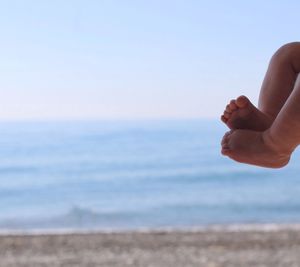 Person hand by sea against sky