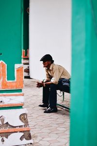 Side view of man sitting on bench at footpath