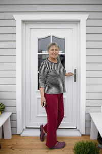 Smiling senior woman standing on porch of her house