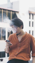 Young man using mobile phone while smoking outdoors