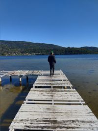 Rear view of man on pier over lake against clear sky